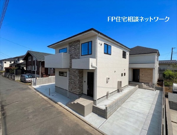外観:白い外壁に石目調のアクセントを取り入れた2階建ての住宅です。前面には広いコンクリート敷きの駐車スペースが設けられ、複数台の駐車に対応。落ち着いた雰囲気の住宅街に建っています。