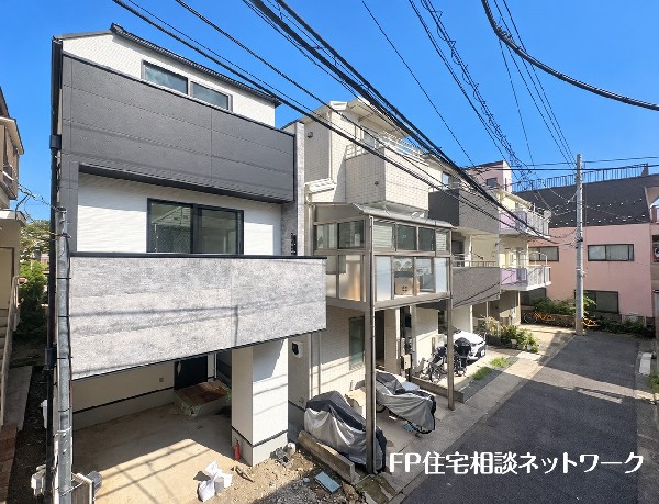 外観:すっきりと晴れ渡った青空の下、モダンなデザインの外観が目を引く一戸建てと、前面に広がる静かな住宅街の道路を撮影した様子です。