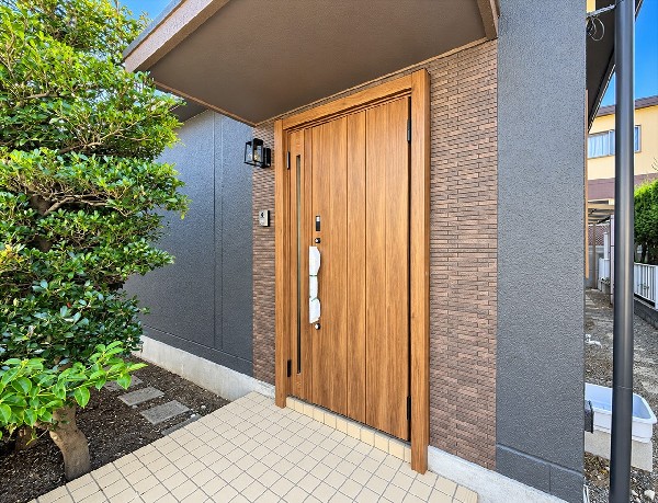外観:木目調の玄関ドアと落ち着いた外壁が迎えるエントランス。軒のある玄関先に緑が彩りを添え、帰宅するたびにほっとする住まいの表情です。