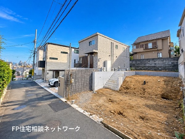 外観:青空が広がる開放的な住宅街に佇む新築邸宅。周辺には落ち着いた街並みが広がり、ゆとりある道路と高低差のある地形が印象的です。